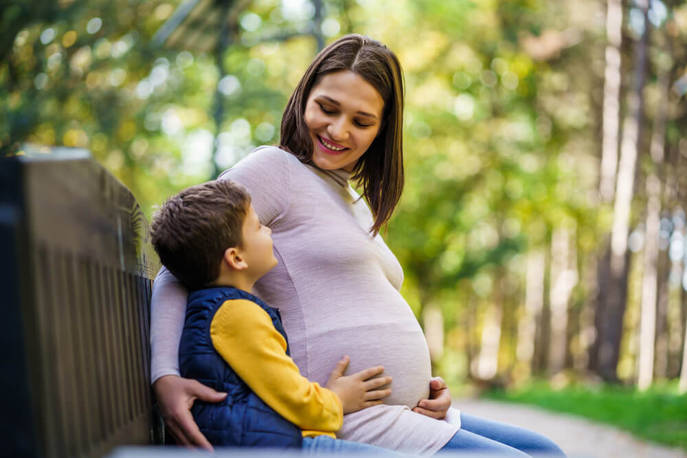 Pregnant mother sitting with son on park bench 